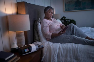 Woman on bed holding her phone, staying up late.
